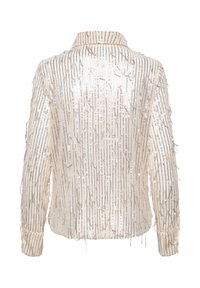 Doorzichtige crèmekleurige blouse met metallic verticale strepen en rafelige textuur. Heeft een kraag en knoopmanchetten. Lichtgewicht stof.