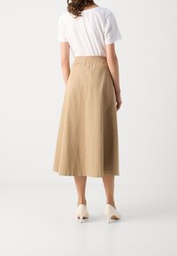 Beige A-linje kjol i lätt material, med elastisk midja och slät yta. Bärs med vit topp och beige klackar.