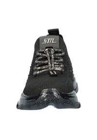 Chaussure de sport en tricot noir avec des lacets décoratifs étincelants, un dessus texturé et une semelle noire brillante présentant un motif en vagues. Marquage argenté sur la languette.
