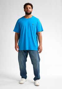 Tricou scurt cu mânecă, de culoare albastru strălucitor, cu decolteu rotund și logo, asortat cu blugi albaștri deschiși și adidași albi. Design simplu, croială lejeră.