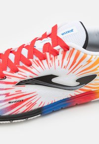 Zapatilla deportiva blanca con cordones rojos, un logo negro y un diseño de degradado multicolor con destellos de acentos naranjas y azules.