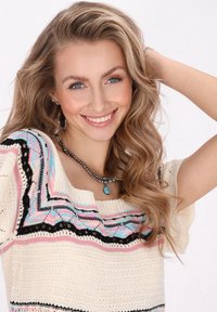 Crème-kleurige gebreide trui met kleurrijke geometrische patronen, korte mouwen en een open halslijn. Accessoires zijn onder andere een gelaagde kralenketting.