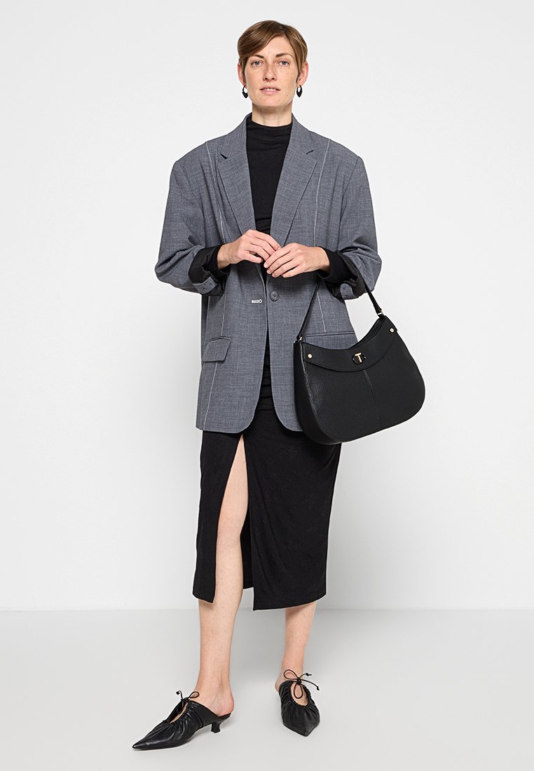 Blazer ancho de cuadros grises, cuello alto negro, falda negra con abertura lateral, bolso negro y zapatos negros puntiagudos con lazos.