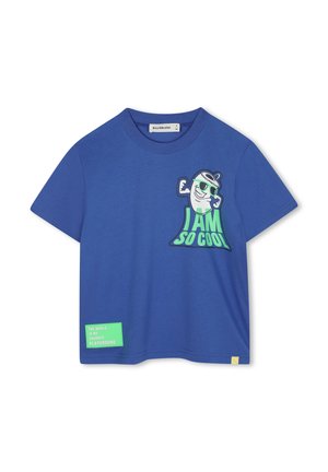T-shirt en coton bleu avec un grand graphisme d'un personnage de dessin animé musclé et le texte "JE SUIS TELLEMENT COOL." Comprend une étiquette verte avec la mention "LE MONDE EST MON PARC DE LOISIRS PRÉFÉRÉ."