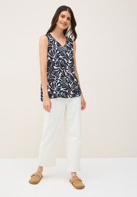 Top senza maniche di colore blu scuro con un motivo a foglie bianche, caratterizzato da scollo a V e vestibilità ampia. Abbinato a pantaloni bianchi a gamba larga e scarpe slip-on beige.