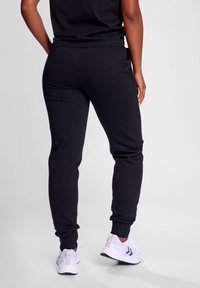 Schwarze Jogginghose aus weichem Material, mit elastischen Bündchen und einer lockeren Passform. Kombiniert mit weißen Sportschuhen für einen Kontrast.