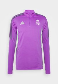 Långärmad sporttopp i lila med kvartszipp, mintgröna detaljer, tre svarta ränder på axlarna och Real Madrids logotyp på bröstet.
