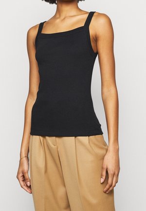 Débardeur noir à côtes avec encolure carrée et bretelles épaisses, forme ajustée, texture lisse, associé à un pantalon plissé beige.