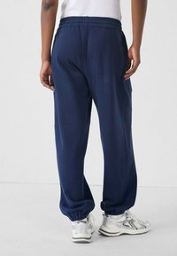 Pantalones de chándal de corte relajado en azul marino con cintura elástica y puños, que cuentan con bolsillos laterales y una suave y lisa mezcla de algodón.