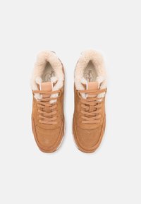 Beżowe zamszowe trampki z puszystym kremowym wnętrzem, sznurowane, z białą podeszwą i subtelnymi detalami przeszyć. Logo widoczne na wkładkach.