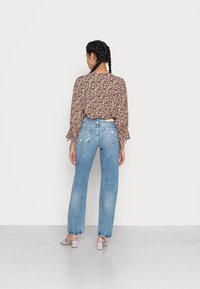 Blusa floral com corte solto, mangas longas com babados. Jeans reto de cintura alta em azul claro com detalhes desgastados, usados com sapatos de bloco em lavanda.