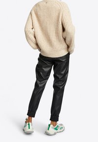 Gruby, kremowy sweter dzianinowy, czarne spodnie z sztucznej skóry i białe trampki z zielonymi akcentami. Teksturowany sweter i marszczone mankiety spodni.