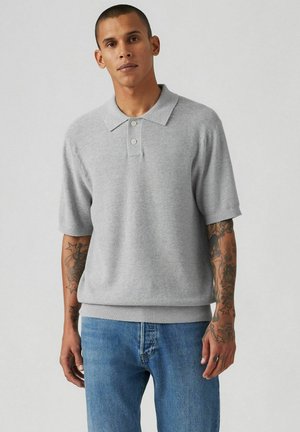 Lys grå kortærmet polo skjorte med klapkrave og tre knapper. Fremstillet af et blødt stof, har ribbet kant og manchetter.