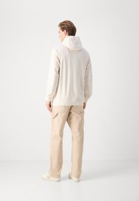 Sudadera con capucha de color beige claro con textura acanalada, combinada con pantalones cargo beige que cuentan con bolsillos laterales y dobladillos ajustados. Zapatillas blancas completan el conjunto.