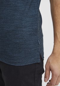 Navyblaues T-Shirt aus strukturiertem Stoff, mit abgerundetem Saum, leichten seitlichen Schlitzen und einem kleinen Logolabel auf der linken Unterseite.