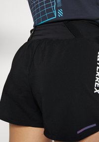 Svarta sportshorts i lättviktsmaterial med elastisk midja, en sidoficka med dragkedja och en lila och vit logotypaccent.