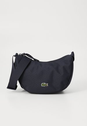 Borsa a spalla in tessuto blu navy con forma curvilinea, tracolla regolabile e logo di coccodrillo ricamato sul fronte. Chiusura con zip superiore.