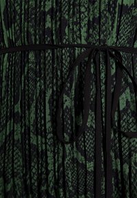 Gros plan sur un tissu imprimé serpent vert et noir avec une fine ceinture noire nouée au centre.