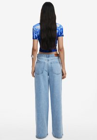 Light blue wide-leg jeans with a faded texture, high waist, and two back pockets. Paired with a fitted, short-sleeve blue top.