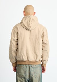 Beige hooded sweatshirt with a relaxed fit, featuring ribbed cuffs and hem, visible stitching, and a smooth textured fabric.