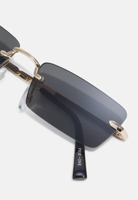 Ochelari de soare cu lentile dreptunghiulare de culoare gri închis, accente din metal aurit și un braț negru pe care este inscripționat "PIER ONE" cu litere albe.