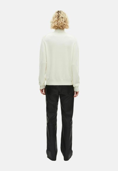 Suéter blanco de punto con cuello alto, combinado con pantalones negros. El suéter tiene un corte holgado y mangas largas, destacando la textura y la simplicidad.
