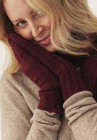 Mănuși tricotate burgundy cu textură cu dungi, asortate cu un pulover bej. Material moale și croială strânsă evidențiază căldura și confortul.