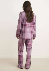 Ensemble de détente à carreaux violets comprenant un haut à manches longues et un pantalon assorti, fabriqué à partir d'un tissu doux avec un motif à carreaux et une coupe décontractée.
