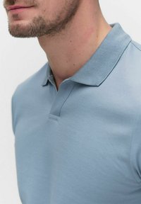 Ljusblå polo av texturerad tyg med krage, med en knapp och en slim fit-design.