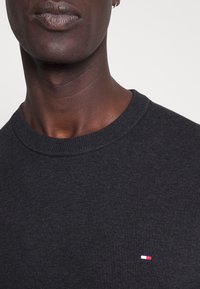 Czarny sweter z dzianiny z rypsowym okrągłym dekoltem i małą wielokolorową naszywką na piersi. Gładka tekstura, dopasowany krój.