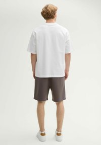 Camiseta blanca de algodón con mangas cortas, combinada con pantalones cortos grises y zapatillas blancas con un acento marrón en el talón.