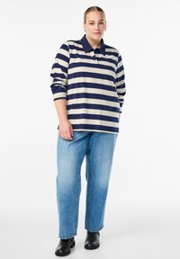 Polo majica z dolgimi rokavi v navy in bež črtah, kombinirana s širokimi modrimi kavbojkami in črnimi gležnjarji. Ima ovratnik in sproščen kroj.