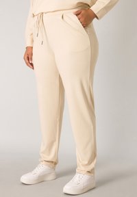 Beige joggingbroeken van een zachte stof, met zijzakken, een drawstring taille en een relaxte pasvorm. Gepaard met witte sneakers.