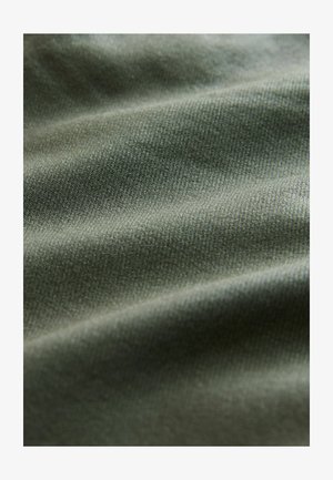 Tume roheline tekstureeritud kangas, millel on pehme ja sile pind ning kerge läige, sisaldab peent diagonaalset kudumismustrit ja õrnu voldikesi.