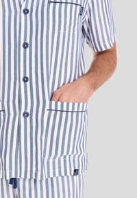 Top de pijama de manga corta a rayas azul y blanca con botones, bolsillo y ribete. Material de algodón con textura suave.