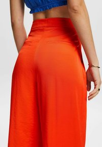 Světlé oranžové široké kalhoty vyrobené z hladké tkaniny, s upraveným pasem a dvěma zadními kapsami, s plochým předním designem.