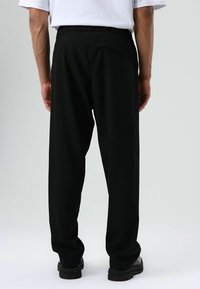 Zwarte broek met elastische tailleband en een losse pasvorm, voorzien van één achterzak en rechte pijpen, gezien vanaf de achterkant.