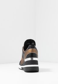 Schwarze und bronzefarbene Sneaker mit strukturiertem Mesh-Material, einer schmalen Form, weißen Sohlen und einem silbernen Akzent an der Ferse.