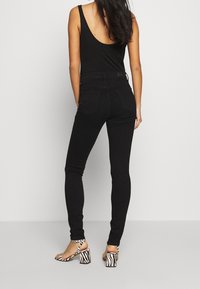 Zwarte high-waisted skinny jeans met een gladde textuur en achterzakken, gecombineerd met zwart-witte gestreepte block-heel sandalen.