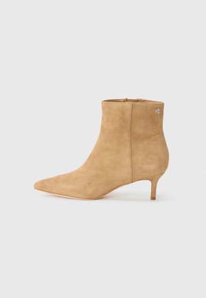 Stivale alla caviglia in suede beige con punta affilata e tacco basso, dotato di chiusura con zip e logo sul retro. Texture liscia.
