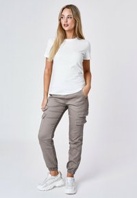 T-shirt bianca con logo in rilievo, abbinata a pantaloni cargo grigi con tasche e polsini elasticizzati, completata da sneakers bianche.