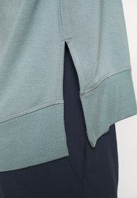 T-shirt a maniche corte in misto cotone verde chiaro, con spacchi laterali e orlo a coste. Abbinato a pantaloni di tessuto blu scuro.