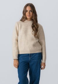 Beige uldtrøje med rund halsudskæring og lange ærmer, der har en blød tekstur. Sammen med blå denim jeans.