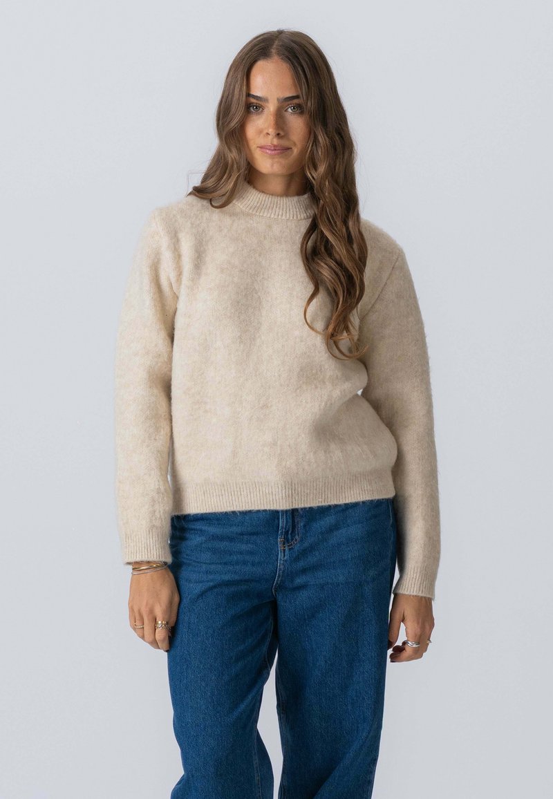 Beige uldtrøje med rund halsudskæring og lange ærmer, der har en blød tekstur. Sammen med blå denim jeans.