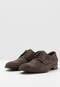 Chaussures habillées en daim marron à lacets avec une texture lisse, des orteils ronds et des lacets noirs contrastants, dotées d'un petit talon empilé.