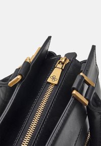 Zwarte leren tas met gouden ritssluiting en gespdetails, deels open om de binnenvakken te tonen.