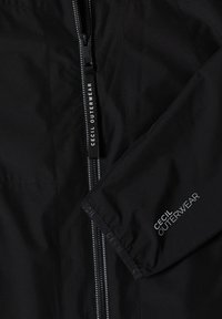 Veste d'extérieur noire avec fermeture éclair visible et manche affichant la marque "Cecil Outerwear" en texte blanc.