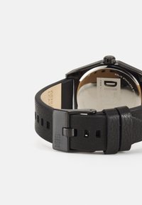Ceas din piele neagră cu carcasă octogonală din oțel inoxidabil, având o brățară netedă, detalii texturate și o cataramă metalică robustă.