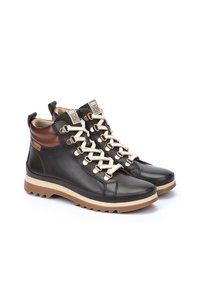 Botas de cuero negras hasta el tobillo con cordones beige, acentos de cuero marrón y suelas de goma texturizada color tostado. Cuenta con herrajes dorados y un collar acolchado.