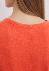 Kortærmet koralfarvet T-shirt med rund hals. Blød tekstur, diskret meleret mønster og en lige søm bagpå.